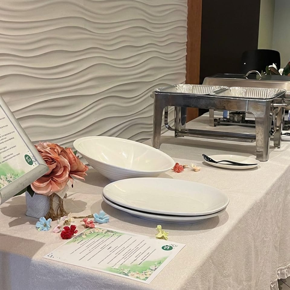 Decorated buffet table with serving trays, white dishes, floral accents, printed menus, and a textured wave-pattern wall.