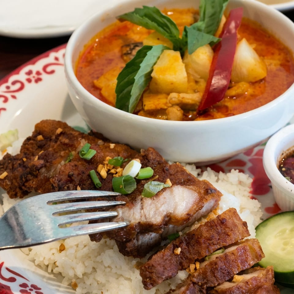 Vietnamese-style platter with white rice, grilled pork, crispy meat, cucumber slices, dipping sauce, and a bowl of red curry.