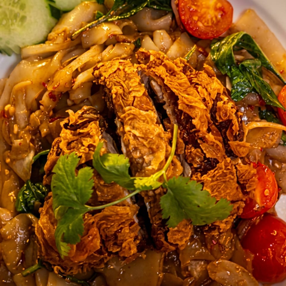 Stir-fried noodles with mushrooms and greens, topped with crispy fried vegetables, cilantro, cherry tomatoes, and cucumber slices.