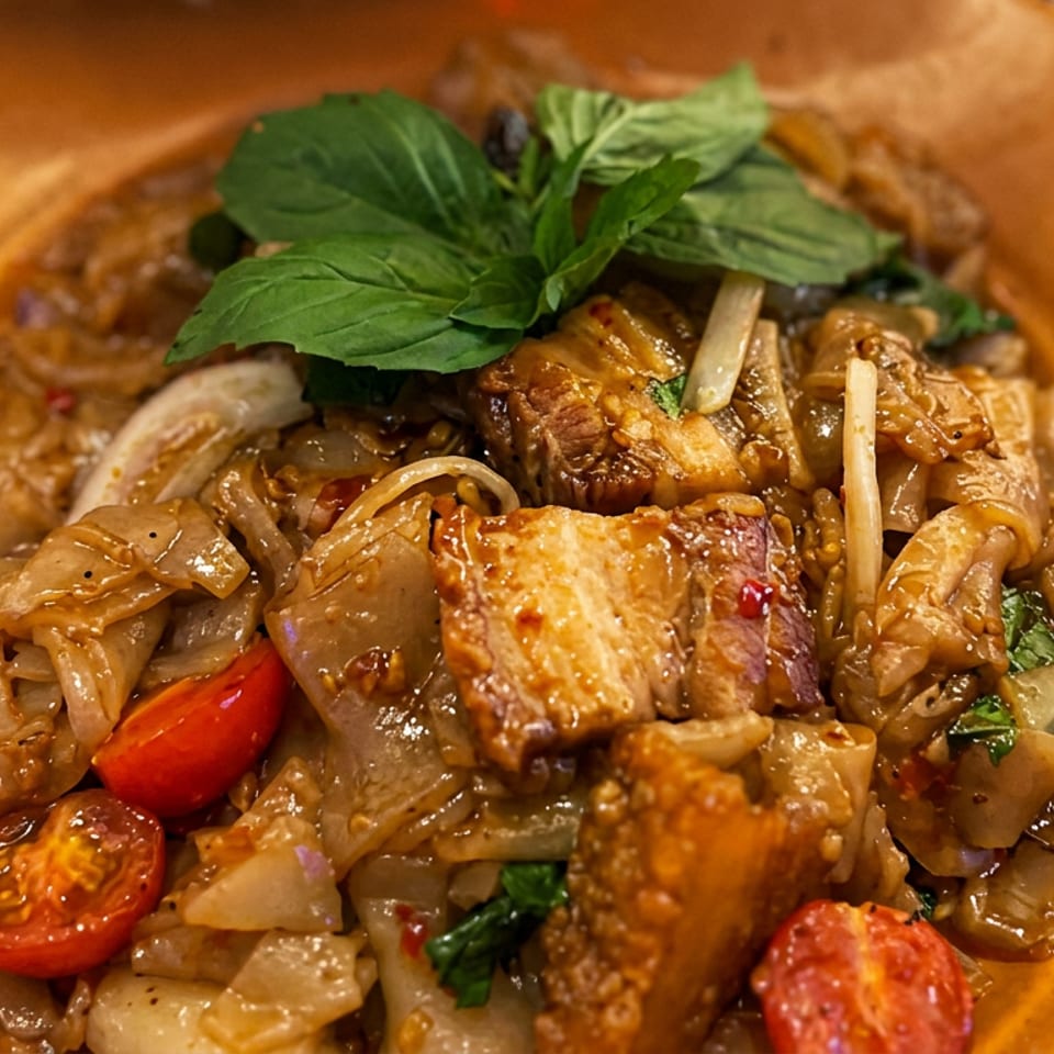 Close-up of a saucy stir-fried dish with tofu, mushrooms, onions, cherry tomatoes, bean sprouts, and fresh basil on an orange plate.