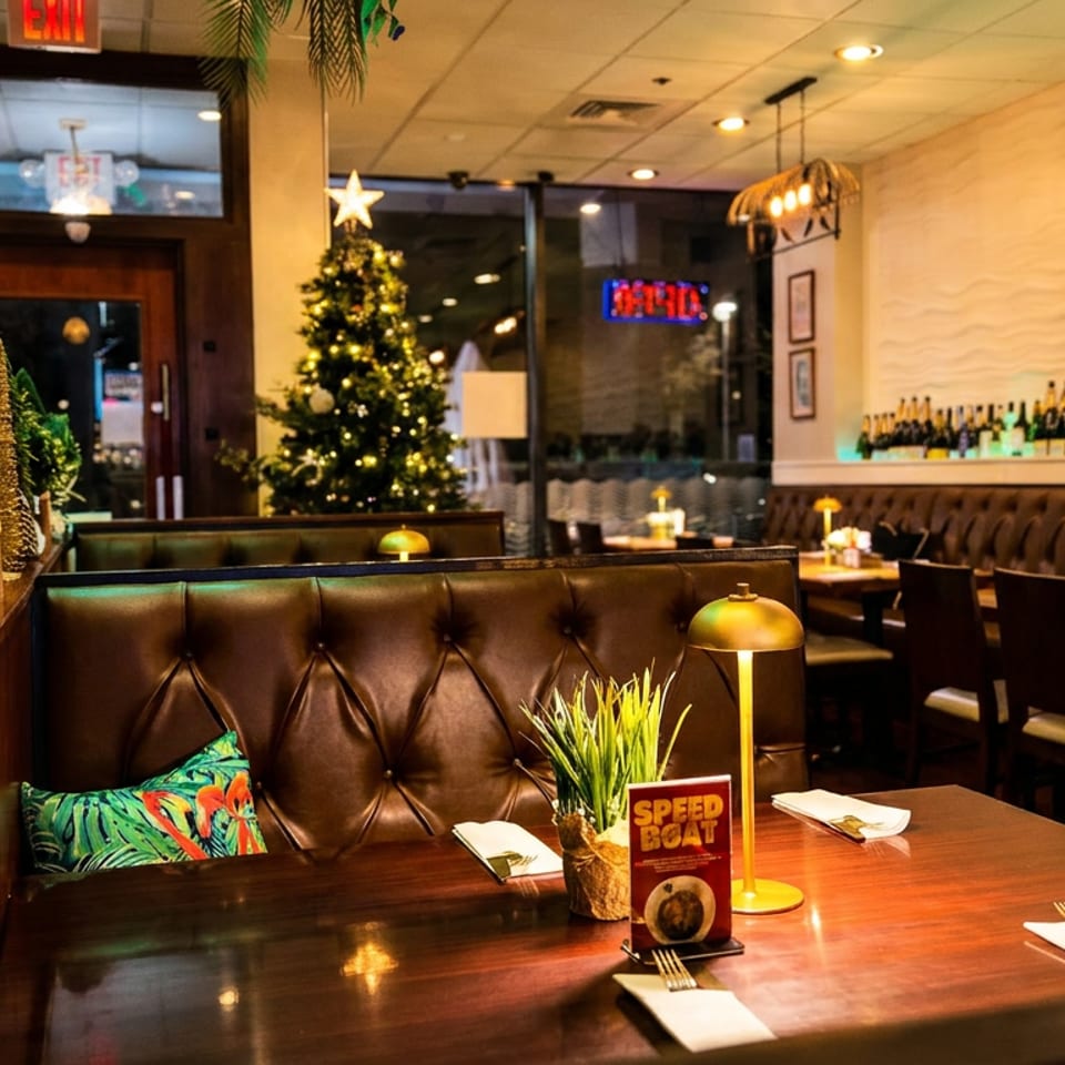 Warmly lit restaurant dining room with leather booths, set tables, festive Christmas trees, hanging birdcage lights, and a bottle-lined wall.