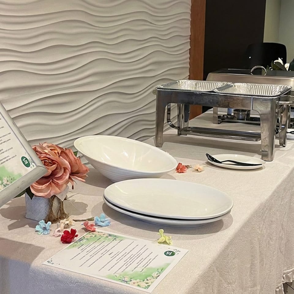 Elegant restaurant buffet table with white linens, serving chafing dishes, empty plates, floral decorations, and menu cards.